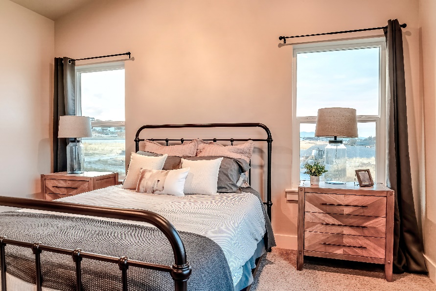 Bedroom with a bed and two side tables in front of two single hung windows.